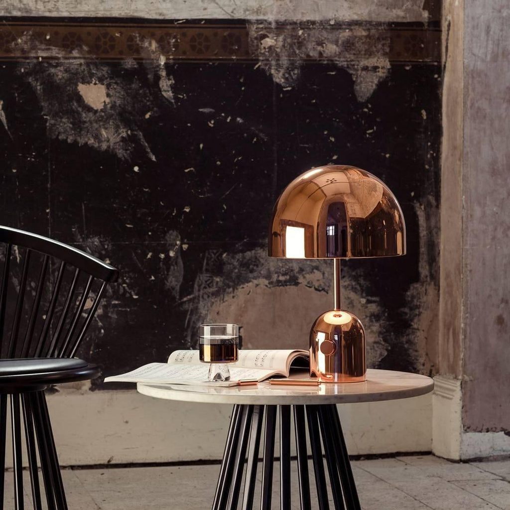 This Clérachic rose gold table lamp's dome shade fills the frame above a marble table and dark plaster wall.