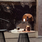 This Clérachic rose gold table lamp's dome shade fills the frame above a marble table and dark plaster wall.