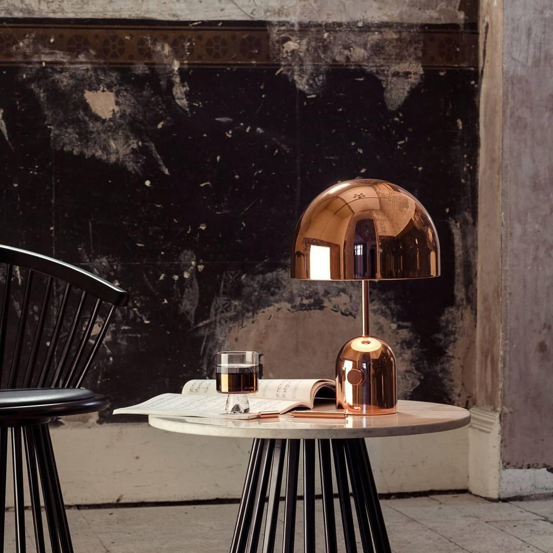 This Clérachic rose gold table lamp's dome shade fills the frame above a marble table and dark plaster wall.