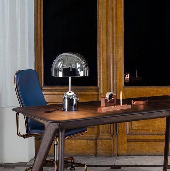 At a wooden desk before tall arched windows, this Clérachic chrome table lamp sits beside small desk accessories.