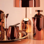 Copper kitchenware and a drum-shade lamp sit on a tray, shown near this Clérachic dome table lamp range in rose gold.