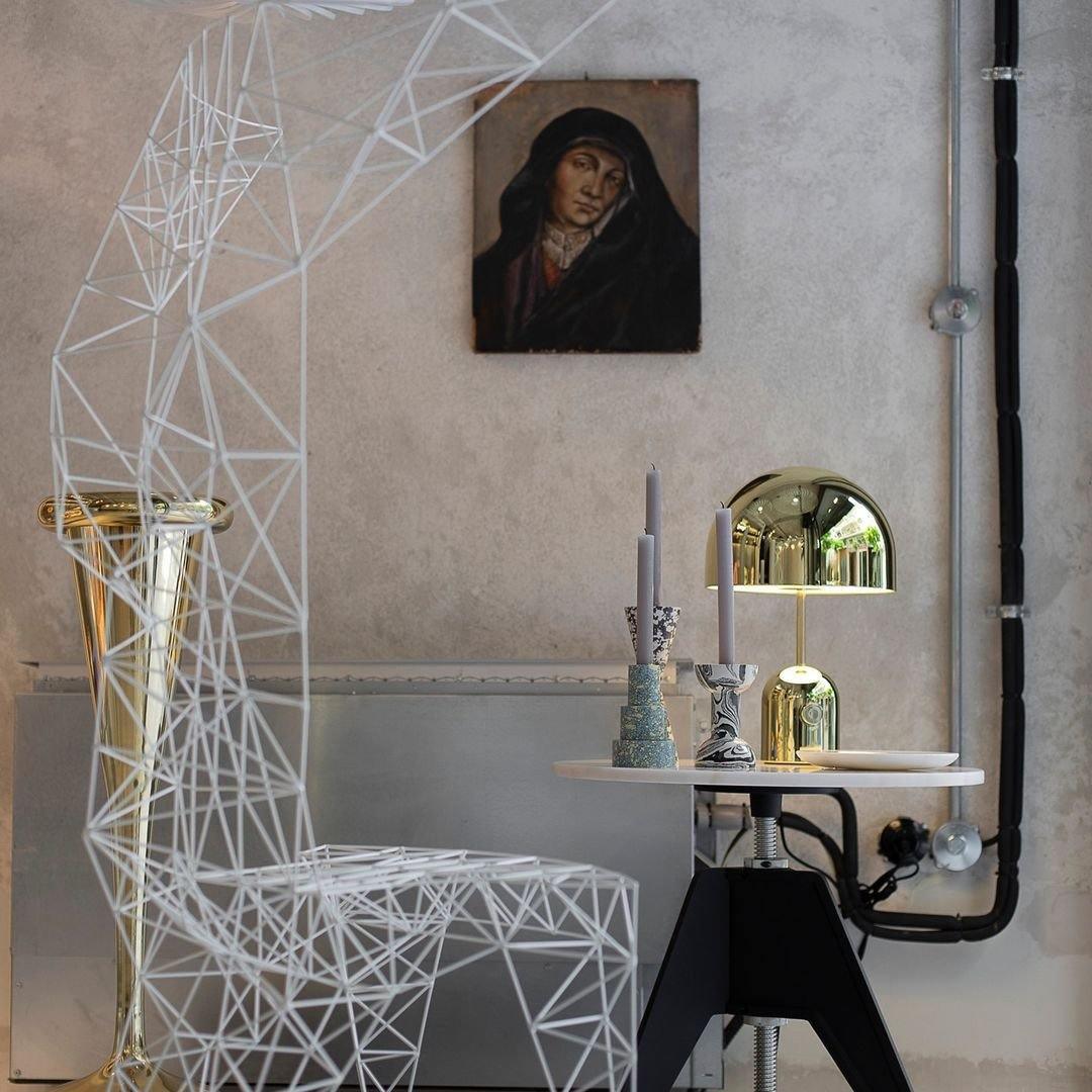 A small dome-topped version of this Clérachic lamp sits on a white pedestal table beside a wire-frame chair and framed portrait.