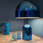 In blue, this Clérachic table lamp stands on a wood table beside small teal figurines of owls and a girl.