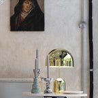 This Clérachic gold table lamp sits beside a pair of taper candles in decorative holders, near a framed portrait.