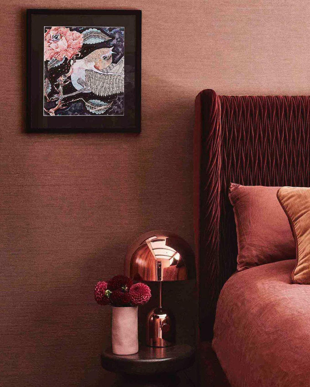 Beside a red velvet headboard, this Clérachic rose gold table lamp sits on a round side table under framed bird art.
