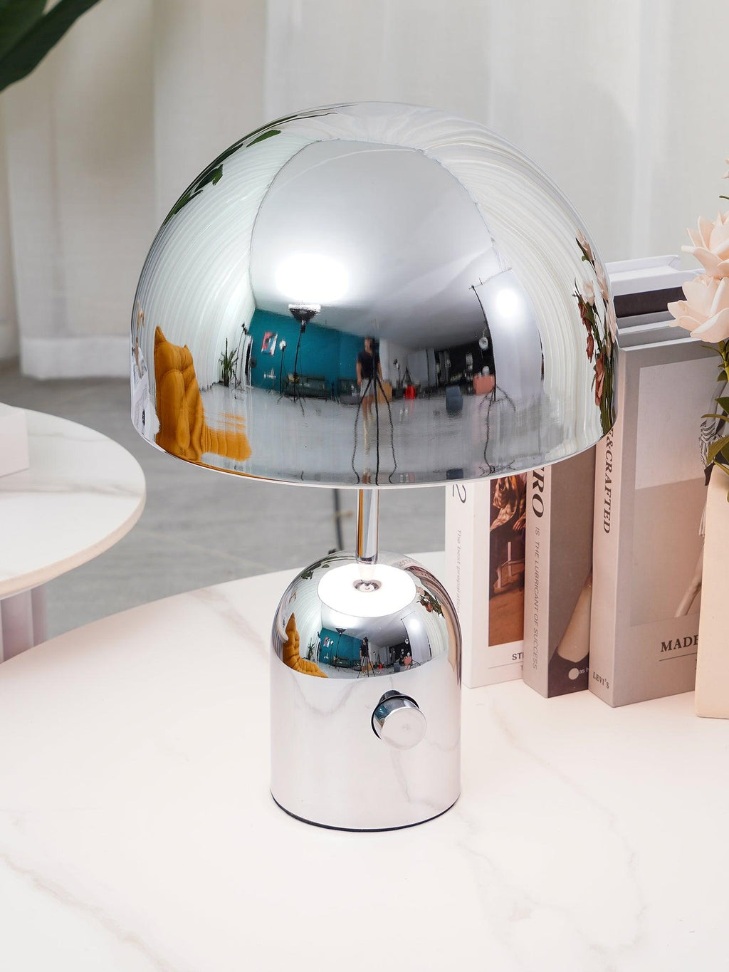 A close view of this Clérachic chrome table lamp's dome shade, reflecting the room, set on a marble table with books.