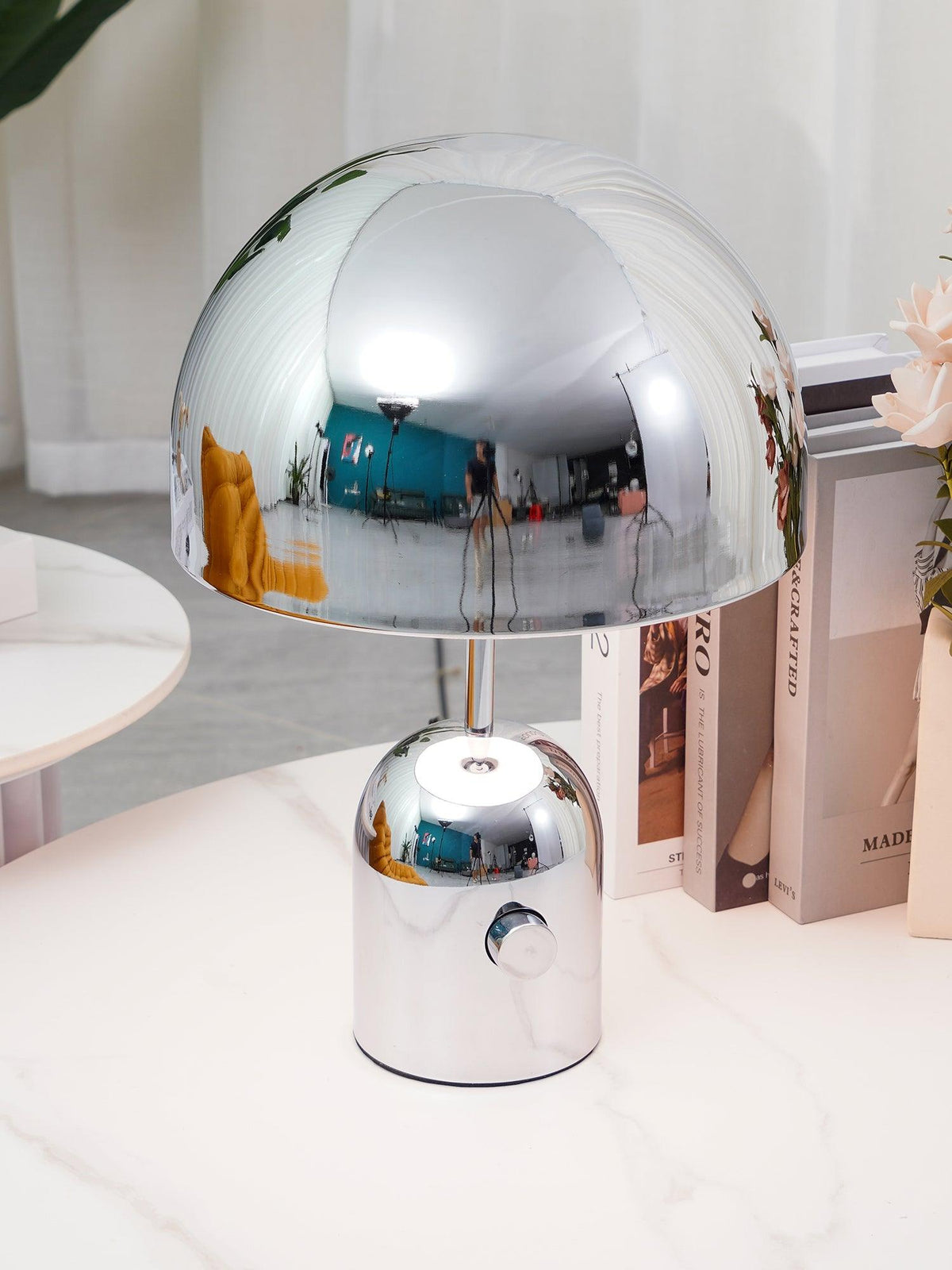 A close view of this Clérachic chrome table lamp's dome shade, reflecting the room, set on a marble table with books.