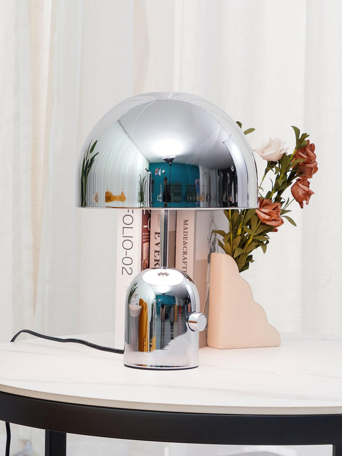Next to a smaller matching lamp, this Clérachic chrome table lamp sits among books and a small vase of flowers.