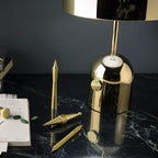 A close view of the push-button switch on this Clérachic gold table lamp, set on a dark marble desk with pens nearby.
