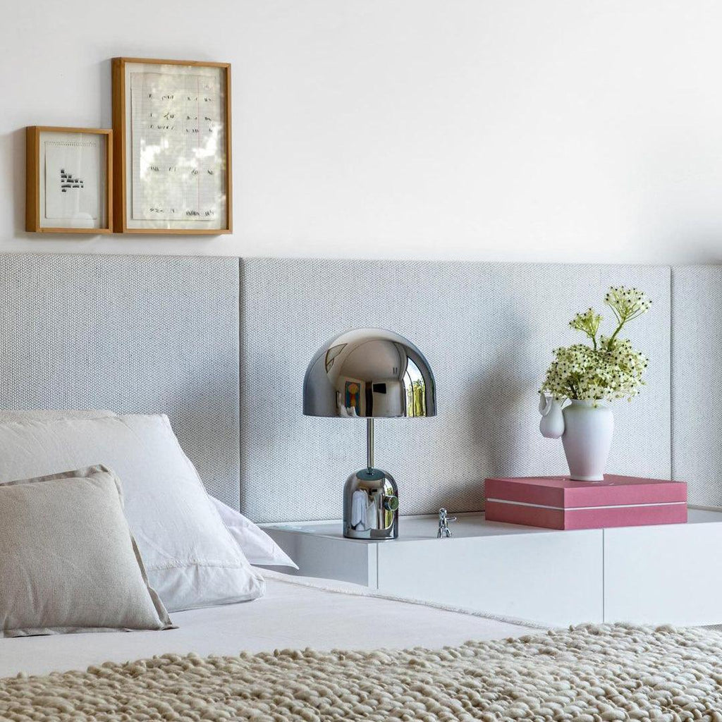 Beside a small vase of greenery, this Clérachic chrome table lamp sits on a white platform nightstand near a grey headboard.