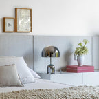 Beside a small vase of greenery, this Clérachic chrome table lamp sits on a white platform nightstand near a grey headboard.