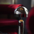 A close-up against deep red velvet shows the dome shade and stem of this Clérachic chrome table lamp.