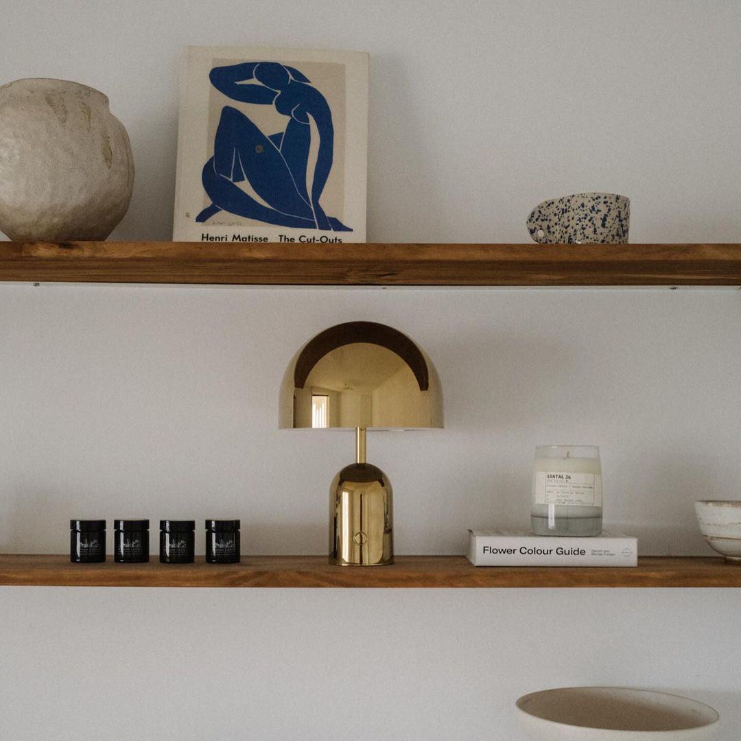 This Clérachic brushed gold table lamp sits on a floating wood shelf beneath a framed Matisse print.