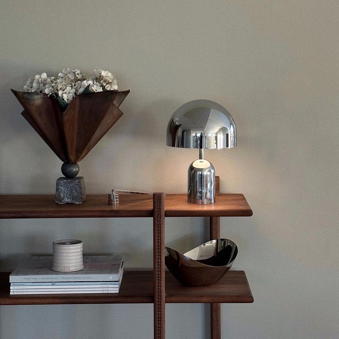 On a wood shelf beside a dried-flower sculpture and stacked books, this Clérachic chrome table lamp stands out.