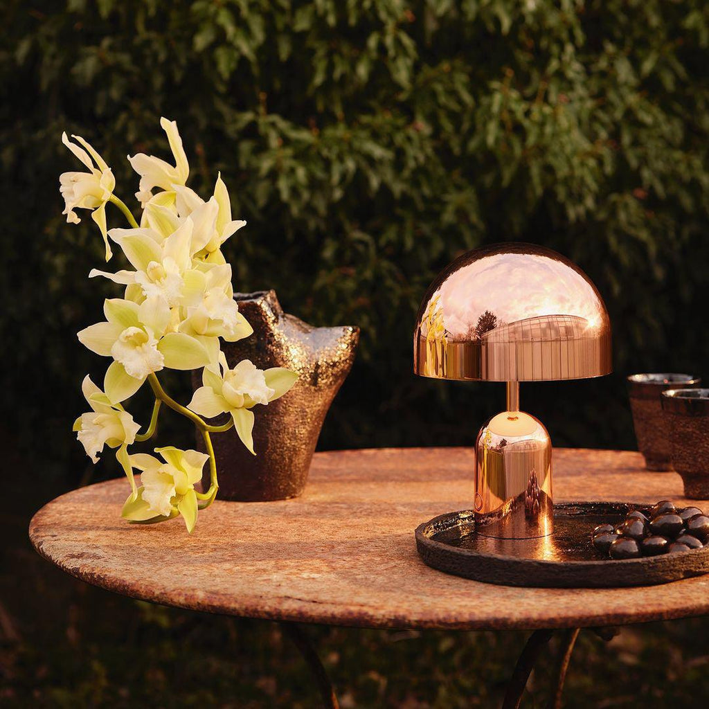 Outdoors on a rustic stone table among yellow orchids, this Clérachic rose gold table lamp catches the daylight.