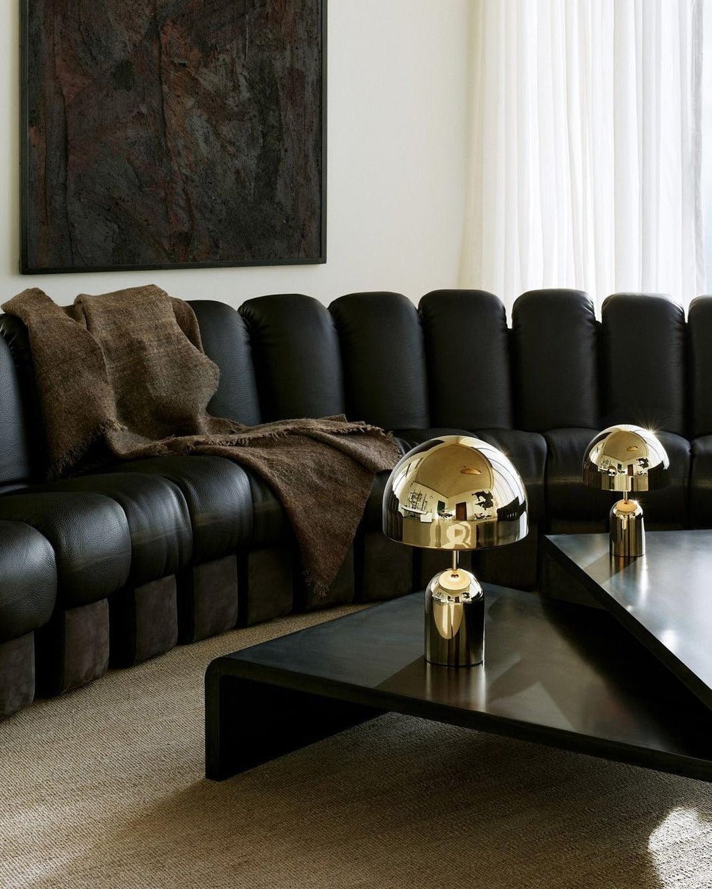 Two sizes of this Clérachic table lamp in chrome sit on a black coffee table before a curved black leather sofa.