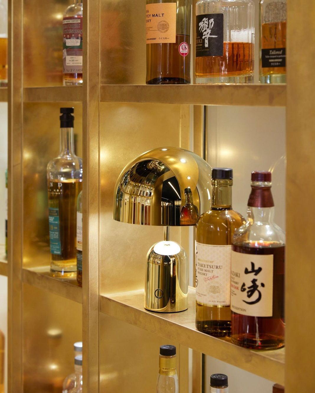 Lit inside a glass bar cabinet, this Clérachic gold table lamp stands among whisky bottles on a glowing shelf.