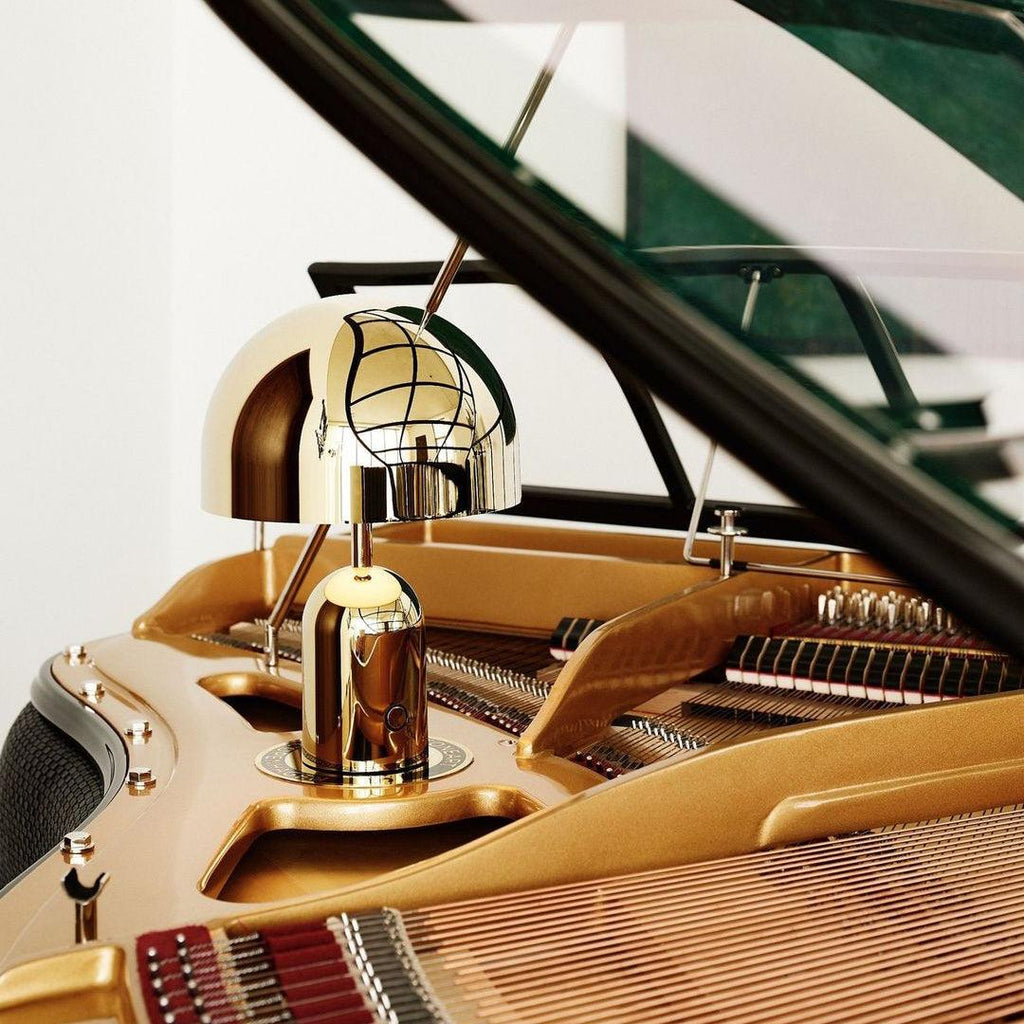 Beside an articulated piano lamp, this Clérachic gold table lamp rests on the open lid of a grand piano.