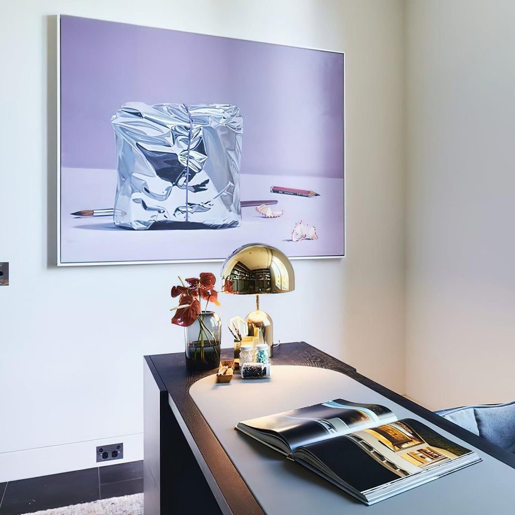 This Clérachic gold table lamp sits on a dark console table below a crumpled silver-foil art print.