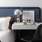 At a white bedroom desk, this Clérachic chrome table lamp stands beside an alarm clock and a pair of headphones.