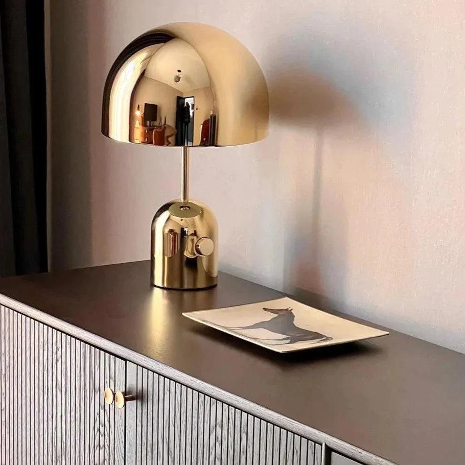 Against a soft pink wall, this Clérachic gold-finish table lamp stands on a dark cabinet with a small tray.