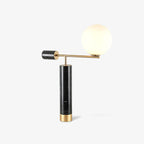 A Clérachic desk lamp on white with a soft shadow beneath its base, the glass globe glowing warm at the top of its arm.