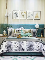 Seen across a bedroom with a teal upholstered headboard and framed leaf prints, the Clérachic desk lamp glows softly on the nightstand.
