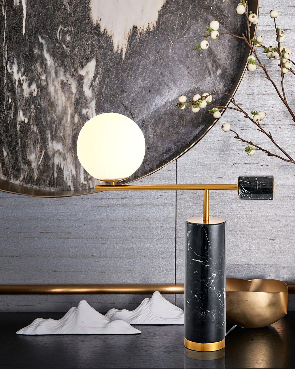 A Clérachic desk lamp is styled against a round mirror with paper mountain props and a gold bowl, its globe lit warm.