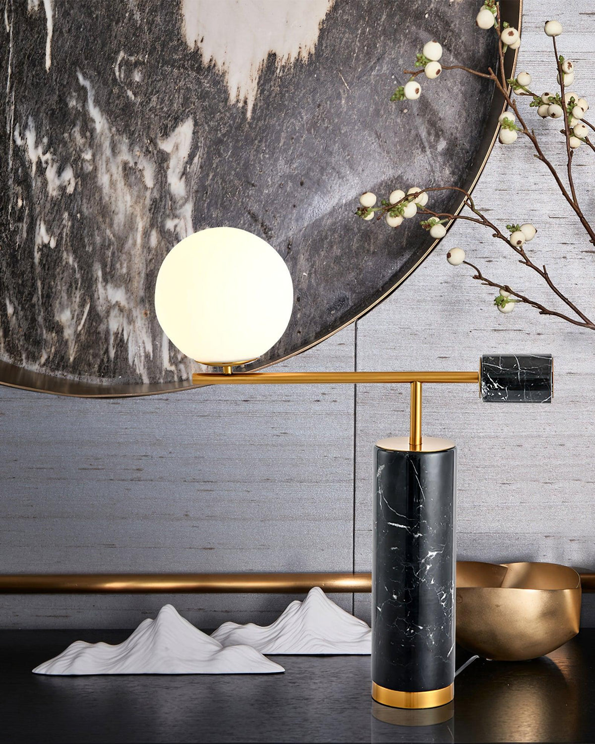 A Clérachic desk lamp is styled against a round mirror with paper mountain props and a gold bowl, its globe lit warm.