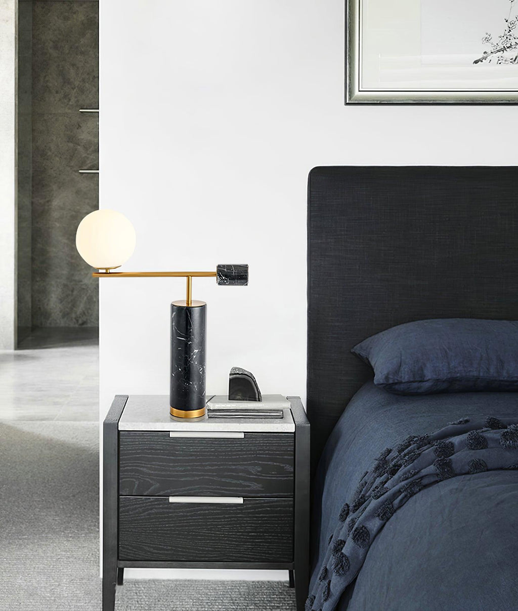 A Clérachic desk lamp glows on a grey nightstand beside a dark upholstered headboard and a phone left charging.