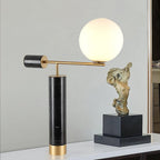 A Clérachic desk lamp with a black marble base stands on a console beside a bronze figure sculpture and dark plinth.