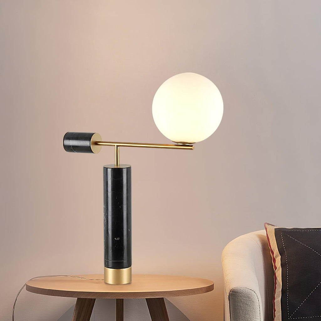 A Clérachic desk lamp glows beside a cream armchair and wooden side table, its warm globe lighting a blush-toned living room.