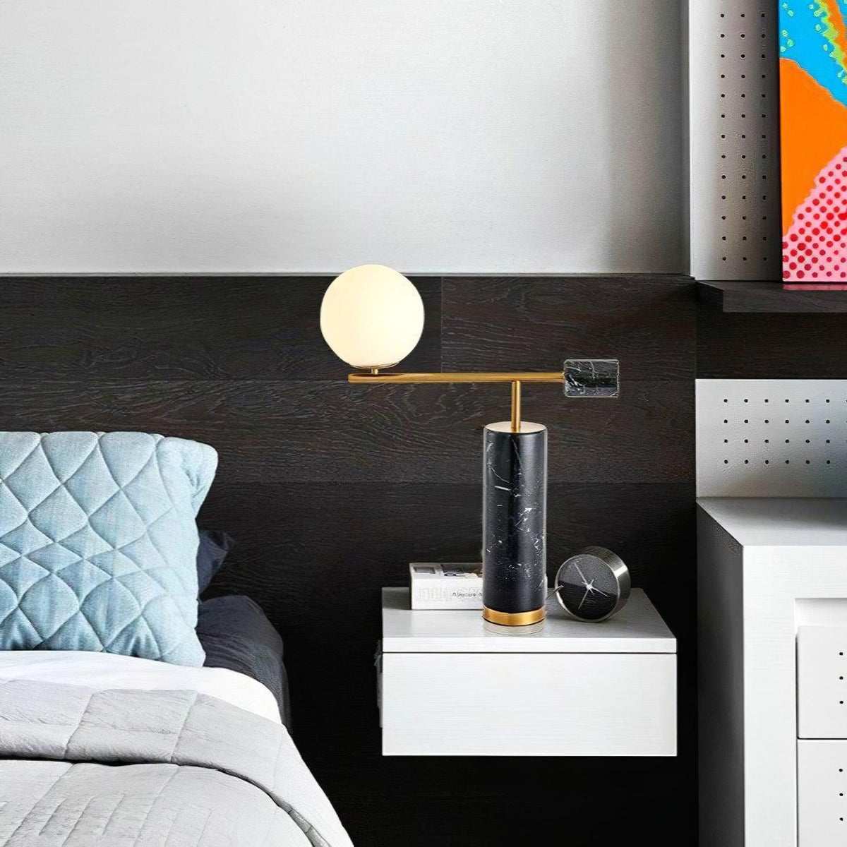 This Clérachic desk lamp lights a dark-panelled bedroom nightstand beside a blue pillow and a round alarm clock.