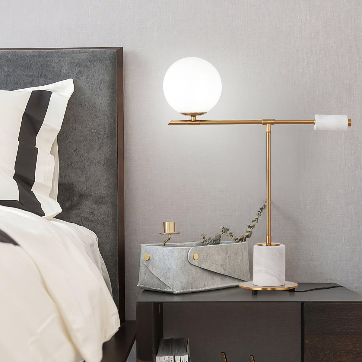 The white-marble Clérachic desk lamp glows on a grey nightstand beside a small woven basket and a trailing plant sprig.