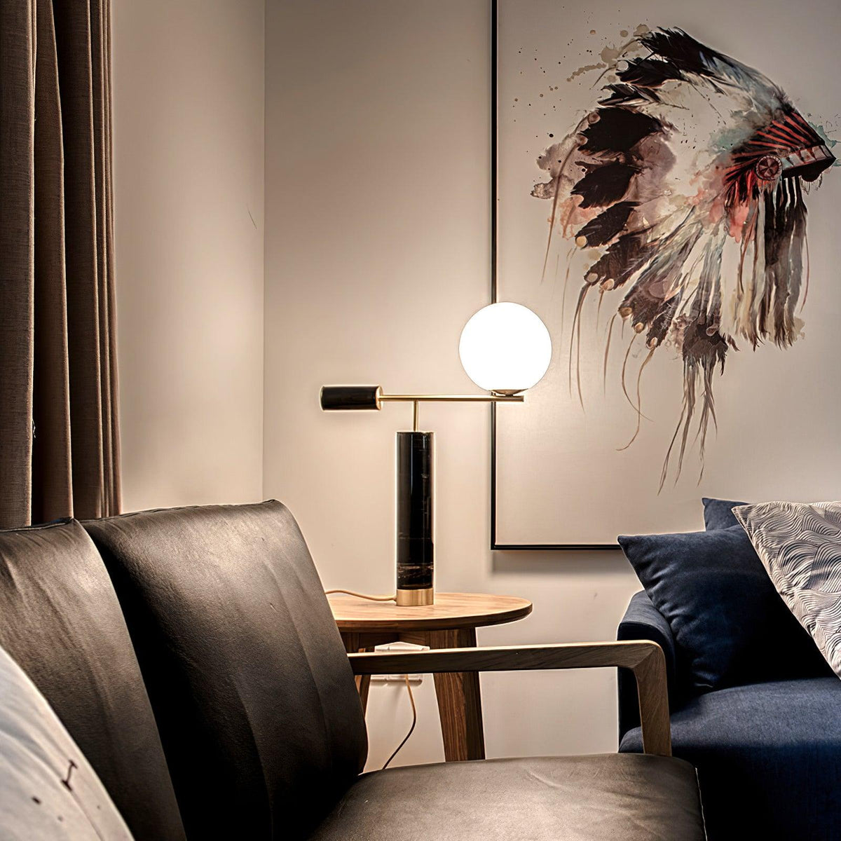 A Clérachic desk lamp glows on a round side table between leather armchairs, beneath a colourful headdress print.