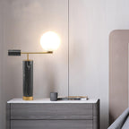 A Clérachic desk lamp glows on a grey dresser beside a mug and folded magazine, with a blush wall behind it.