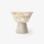 Clérachic bedside table lamp with two pale alabaster cones meeting waist to waist, soft veining crossing the wider upper bowl, shown on a plain grey backdrop.