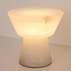 Close crop of the lit Clérachic alabaster table lamp on a wood surface, with no other furniture in view.