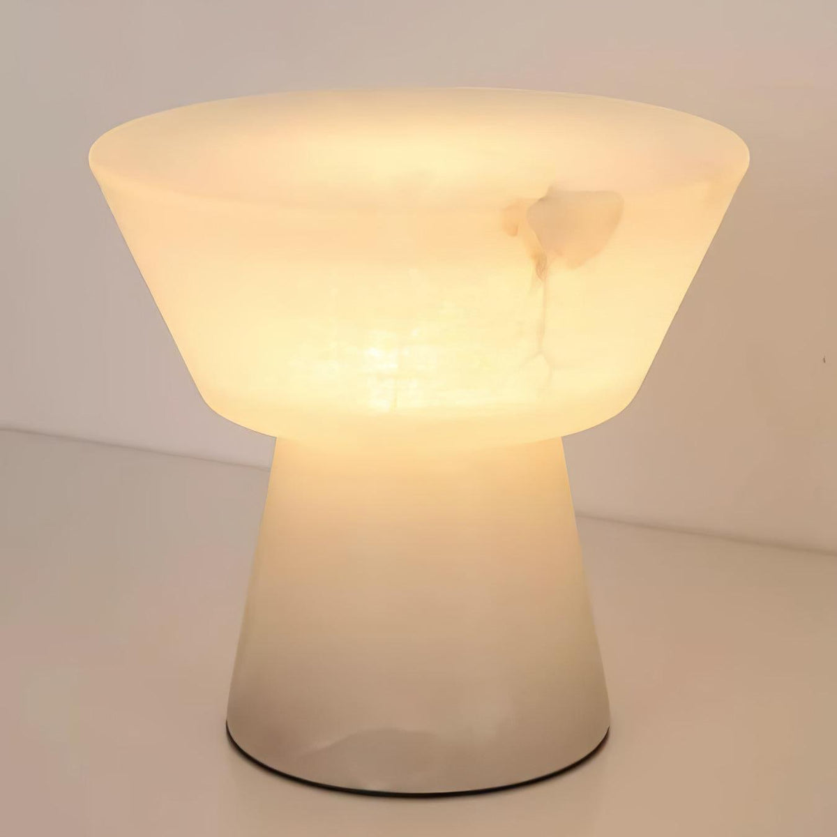Close crop of the lit Clérachic alabaster table lamp on a wood surface, with no other furniture in view.