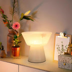 Clérachic alabaster table lamp glowing on an evening counter among cut flowers in small vases and a potted plant.
