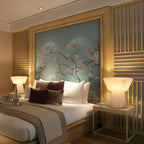 Two Clérachic alabaster table lamps lit in a bedroom with maroon pillows and a gold-framed floral painting.
