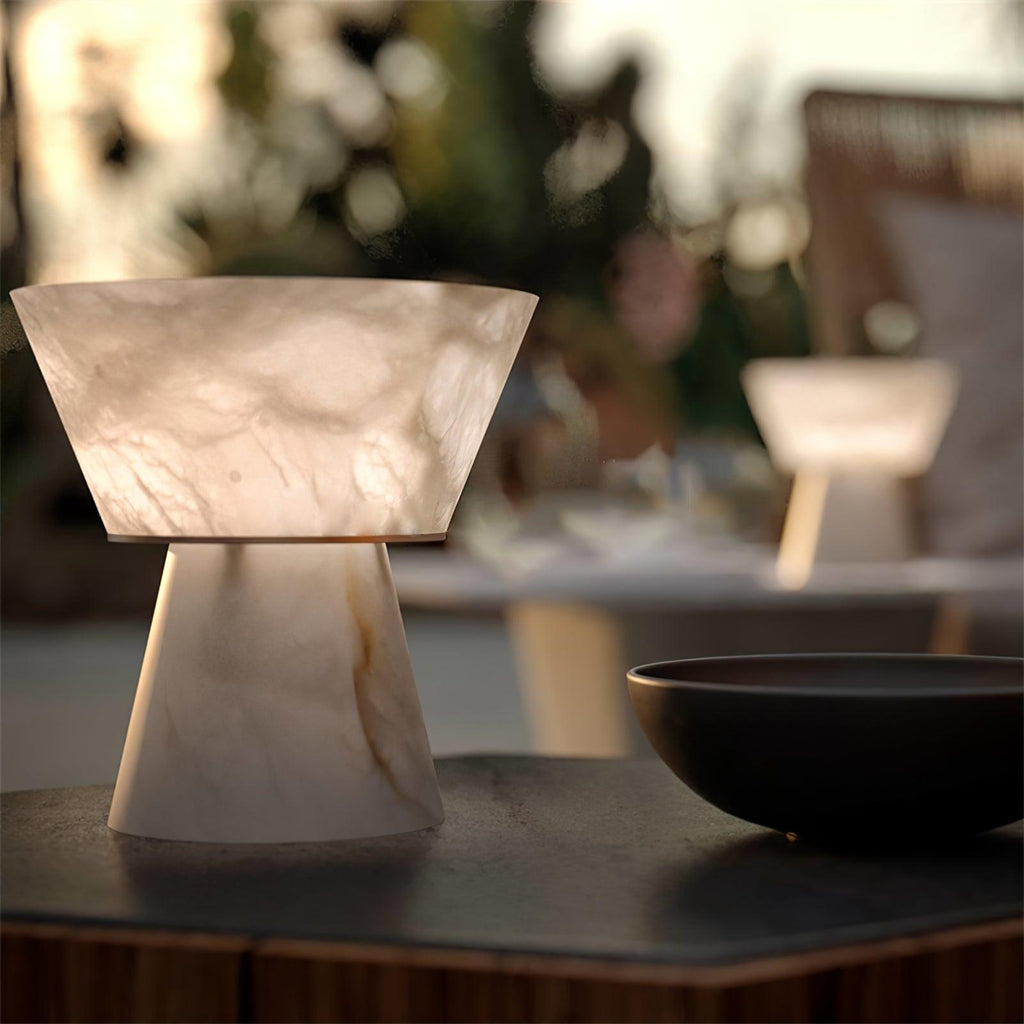 Close crop of the Clérachic alabaster lamp's shade on a dark counter, with a black bowl and blurred greenery behind.