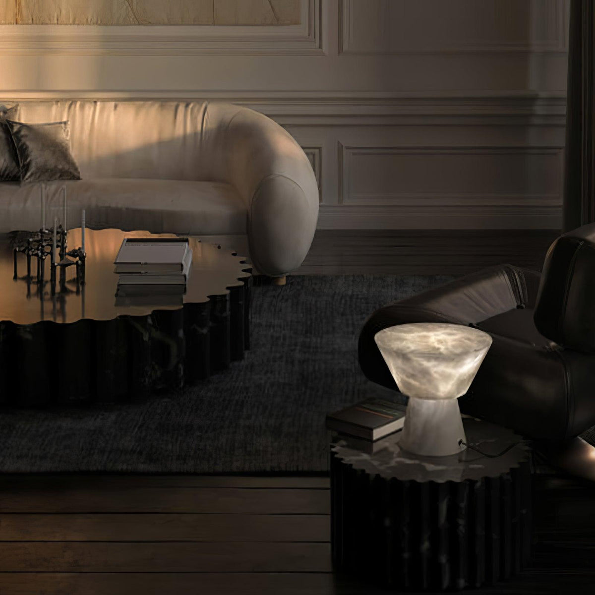 In a moody lounge, the Clérachic alabaster lamp sits lit on a dark round table near a low bench and sofa.