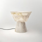 A black power cord trails from the Clérachic alabaster lamp's base across the white studio background.