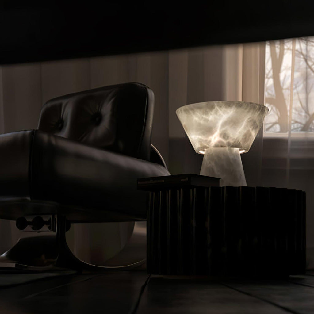 Clérachic alabaster table lamp lit beside a black leather armchair, sheer curtains softening the window light behind it.