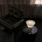 Clérachic alabaster table lamp seen from above on a side table by a black leather armchair, showing the tabletop's grain.