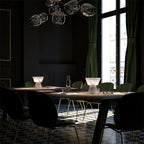 Two Clérachic alabaster table lamps lit on a set dining table with black chairs, pendant lights hanging above them.