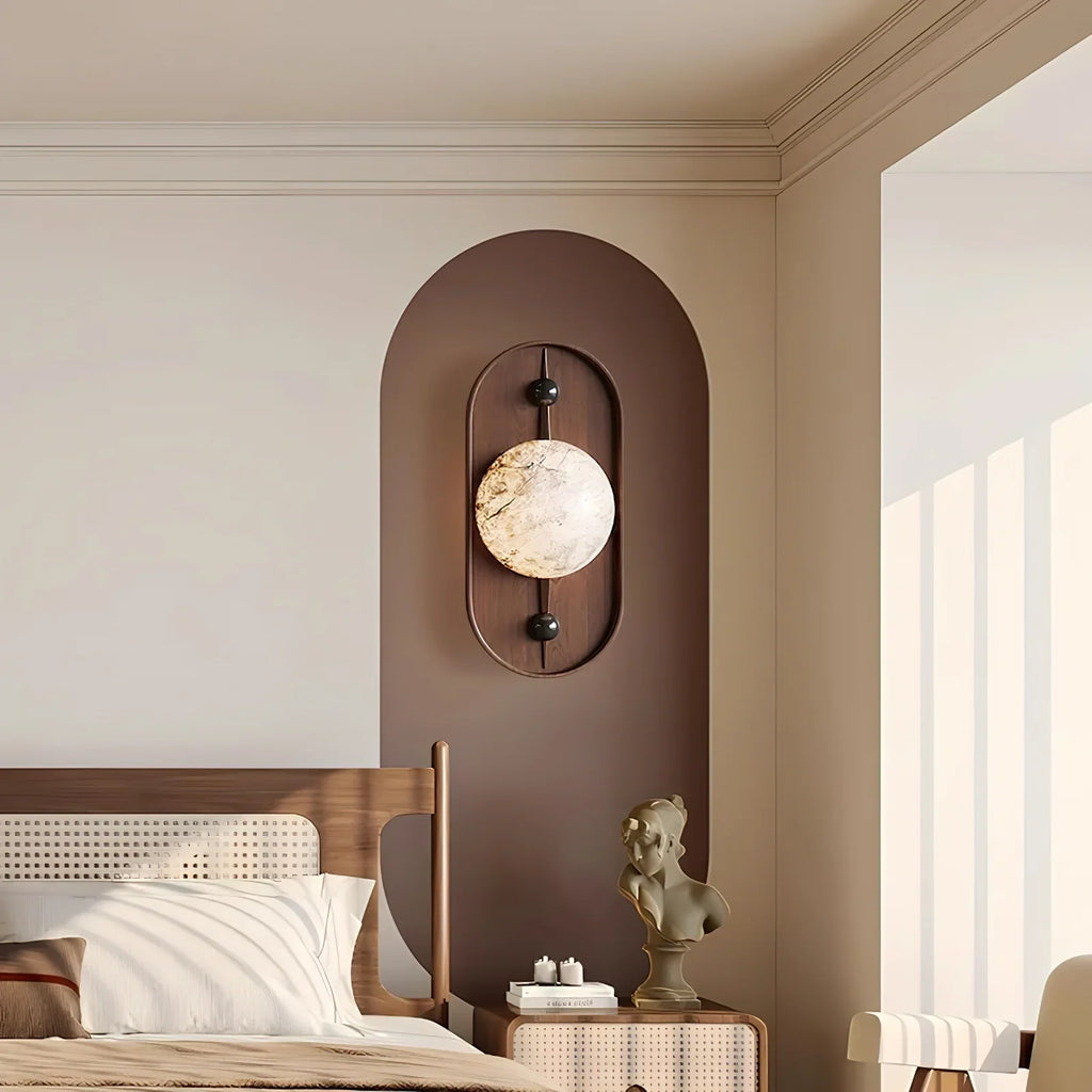 The wall light lit on a brown arched panel in a bedroom, above a rattan bed and a bust sculpture.