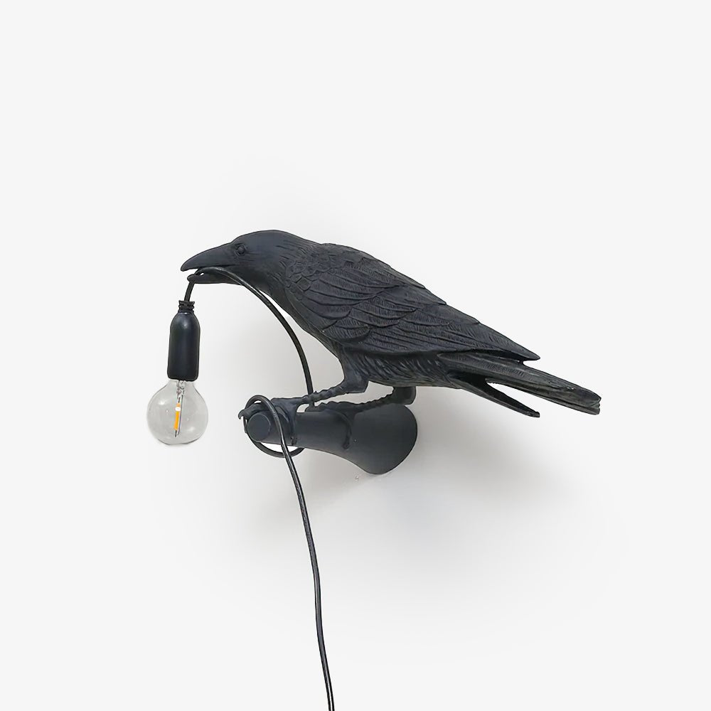 Isolated on light grey, this black Clérachic bird lamp shows its full mount and cord with the bulb glowing warm.