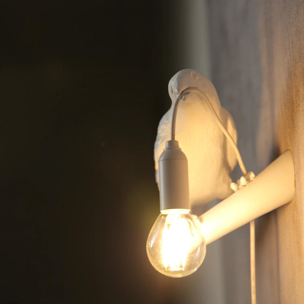 Close view of the glowing filament bulb on this Clérachic bird lamp, the black bird softly blurred against a dark wall.